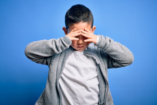 Young little boy kid wearing sport sweatshirt over blue isolated background suffering from headache desperate and stressed because pain and migraine. Hands on head.
