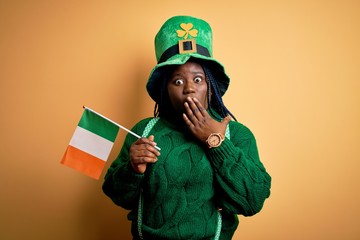 Plus size african american woman wearing green hat holding irish flag on saint patricks day cover...