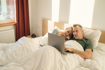 Cheerful couple using a computer lying on their bed at home