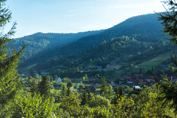 Naklejka na ściany i meble Amazing view of houses and pine-trees in valley of Carpathian mountains in west part of Ukraine. Famous ukrainian mountains. Scenic landscape. Tourist destination for summer and winter holidays