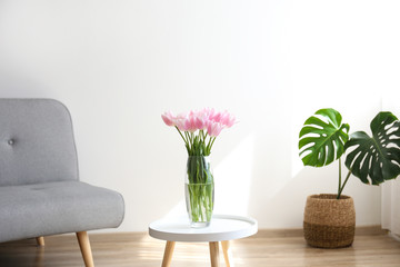 Empty apartment with minimal loft style interior, wooden floor and glass vase with bouquet of tulips on foreground and blank wall with a lot of copy space for text on background. Close up.