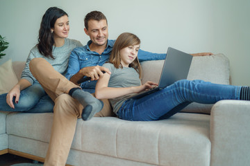 Fototapeta na wymiar Happy family using laptop at home: mom, dad and daughter shopping online or watching funny video or movie