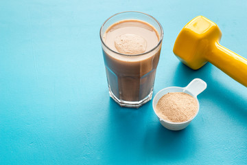 Protein shake in glass near dumbbells on blue background copy space