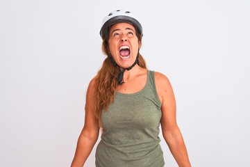 Middle age mature cyclist woman wearing safety helmet over isolated background angry and mad screaming frustrated and furious, shouting with anger. Rage and aggressive concept.