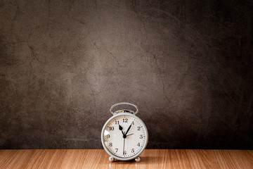 Alarm clock on wooden table with old gray concrete wall for background.