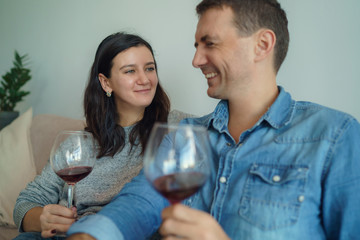 Young romantic couple sitting on sofa at home drinking red wine.