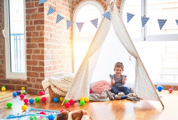 Beautiful toddler sitting on the floor inside tipi applauding and smiling at kindergarten