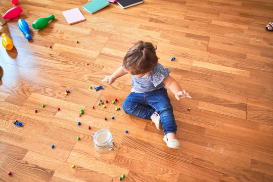 Beautiful toddler sitting on the floor with jar of chocolate colored balls at kindergarten