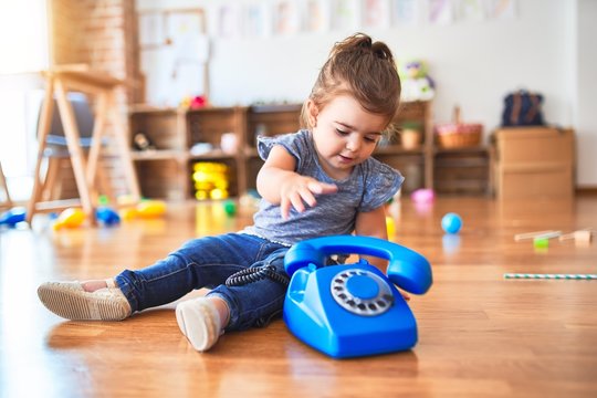 Beautiful toddler sitting on the floor playing with vintage phone at kindergarten
