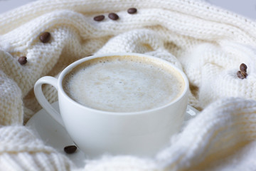 White coffee cup with plate, cofee beans and knitted scarf.