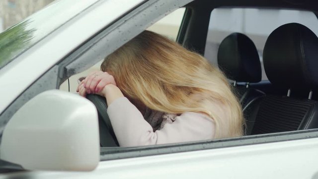 Young blonde woman sitting in a car, puts her hands and head on the steering wheel, disappointment and sadness, fatigue, emotional exhaustion, stress, lack of sleep, problems at work