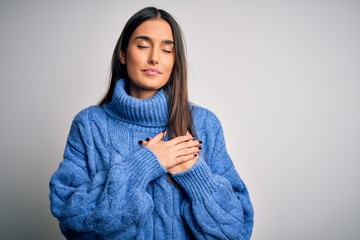 Young beautiful brunette woman wearing casual turtleneck sweater over white background smiling with hands on chest with closed eyes and grateful gesture on face. Health concept.