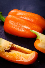 Orange sweet bell pepper cut, focus in the background is sleeping pepper with drops, close-up on a dark background.