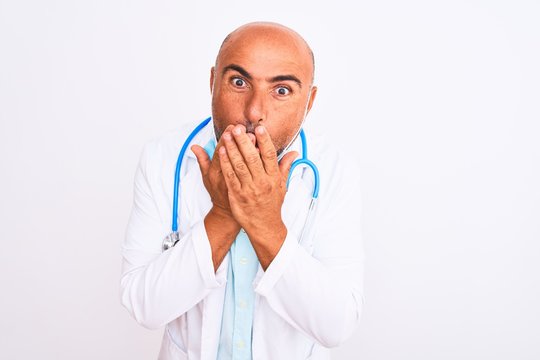 Middle age doctor man wearing stethoscope and mask over isolated white background shocked covering mouth with hands for mistake. Secret concept.