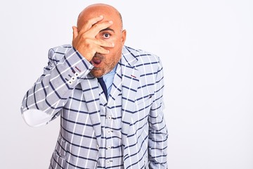 Middle age businessman wearing suit standing over isolated white background peeking in shock covering face and eyes with hand, looking through fingers with embarrassed expression.