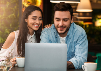 Cheerful Couple Using Laptop Having Coffee Sitting In Cafe