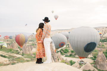 Woman and man watching colorful hot air balloons flying over the valley at Cappadocia, Turkey. 