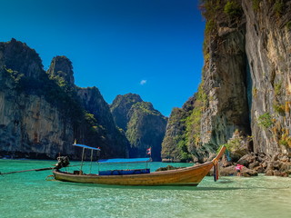 view of a long-tail boat floating in blue-green sea around with high rock mountains and blue sky background, Ao Loh Samah, Mu Ko Phi Phi islands, Krabi, southern of Thailand.