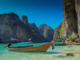 Naklejka na ściany i meble view of a long-tail boat floating in blue-green sea around with high rock mountains and blue sky background, Ao Loh Samah, Mu Ko Phi Phi islands, Krabi, southern of Thailand.