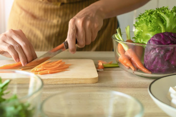 Hand is using knife cutting carrots and have a purple cauliflower cup in to next to it. The preparation for the vegetable salad menu is a healthy diet. For weight loss.Selective focus