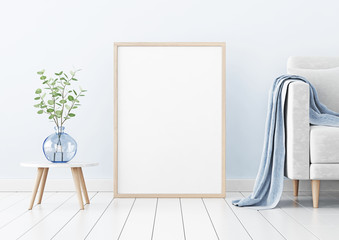 Poster mockup with vertical wooden frame standing on floor in living room interior with sofa and branches in blue vase on empty wall background. 3D rendering, illustration.