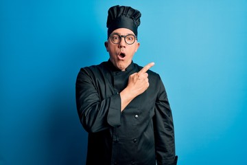 Middle age handsome grey-haired chef man wearing cooker uniform and hat Surprised pointing with finger to the side, open mouth amazed expression.
