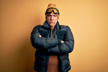 Middle age handsome grey-haired skier man on vacation wearing ski goggles skeptic and nervous, disapproving expression on face with crossed arms. Negative person.