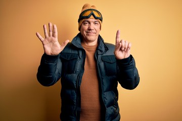 Middle age handsome grey-haired skier man on vacation wearing ski goggles showing and pointing up with fingers number six while smiling confident and happy.