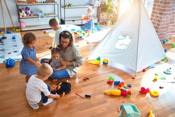 Beautiful teacher and group of toddlers playing around lots of toys at kindergarten