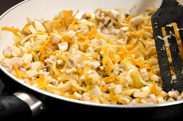 Cooking vegetable stew with mushrooms: onions, carrots and mushrooms are fried in a pan.