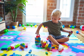 Young caucasian kid playing at kindergarten with toys. Preschooler boy happy at playroom.