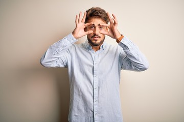 Young handsome man with beard wearing striped shirt standing over white background Trying to open eyes with fingers, sleepy and tired for morning fatigue