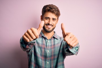 Fototapeta premium Young handsome man with beard wearing casual shirt standing over pink background approving doing positive gesture with hand, thumbs up smiling and happy for success. Winner gesture.