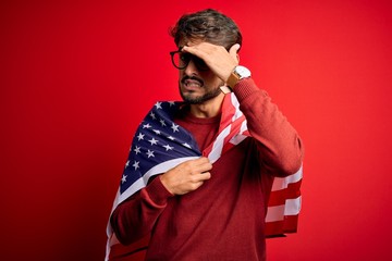 Young man wearing glasses and United States of America flag over isolated red background stressed with hand on head, shocked with shame and surprise face, angry and frustrated. Fear and upset 
