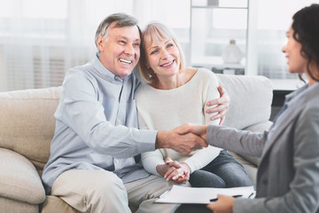 Female realtor handshaking happy mature couple at office