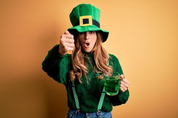 Beautiful woman wearing hat drinking jar of green beverage celebrating saint patricks day annoyed and frustrated shouting with anger, crazy and yelling with raised hand, anger concept