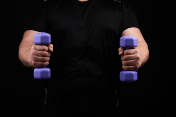adult male athlete in black uniform holds blue plastic blue dumbbells in hands
