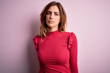 Obraz premium Young beautiful brunette woman wearing casual sweater stnding over pink background with serious expression on face. Simple and natural looking at the camera.
