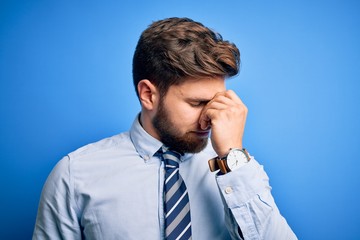 Young blond businessman with beard and blue eyes wearing elegant shirt and tie standing tired rubbing nose and eyes feeling fatigue and headache. Stress and frustration concept.