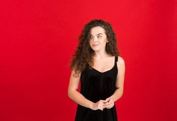 Pretty curly girl in black dress looking away isolated on red background