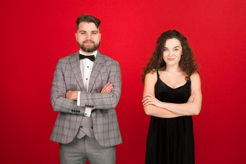 Front view of well dressed smiling couple standing with folded arms isolated on red background