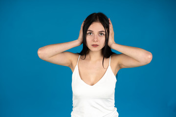 Fototapeta na wymiar Front view of brunette girl covering ears with hands isolated on blue background