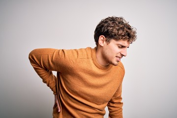 Young blond handsome man with curly hair wearing casual sweater over white background Suffering of backache, touching back with hand, muscular pain