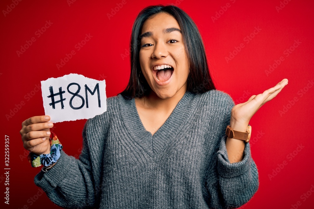 Wall mural Young beautiful asian woman celebrating 8th march womens day holding reminder paper very happy and excited, winner expression celebrating victory screaming with big smile and raised hands