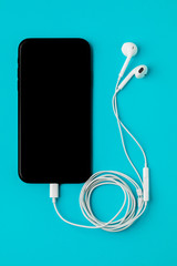 Smartphone with headphones on a blue background. The view from the top. Listen to music
