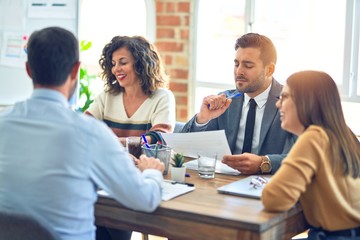 Group of business workers smiling happy working together. Sitting on desk with smile on face reading documents at the office