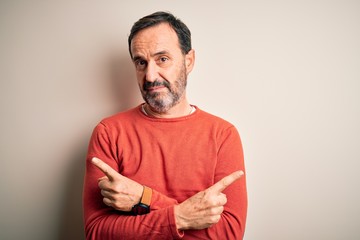 Middle age hoary man wearing casual orange sweater standing over isolated white background Pointing to both sides with fingers, different direction disagree