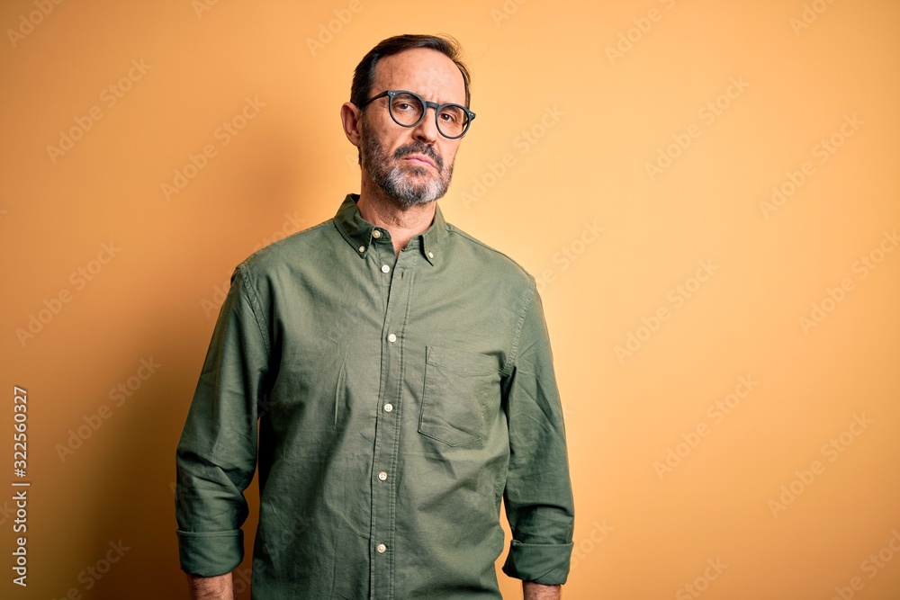 Wall mural Middle age hoary man wearing casual green shirt and glasses over isolated yellow background Relaxed with serious expression on face. Simple and natural looking at the camera.