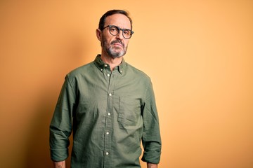 Middle age hoary man wearing casual green shirt and glasses over isolated yellow background Relaxed with serious expression on face. Simple and natural looking at the camera.