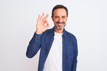 Middle age handsome man wearing blue denim shirt standing over isolated white background smiling positive doing ok sign with hand and fingers. Successful expression.